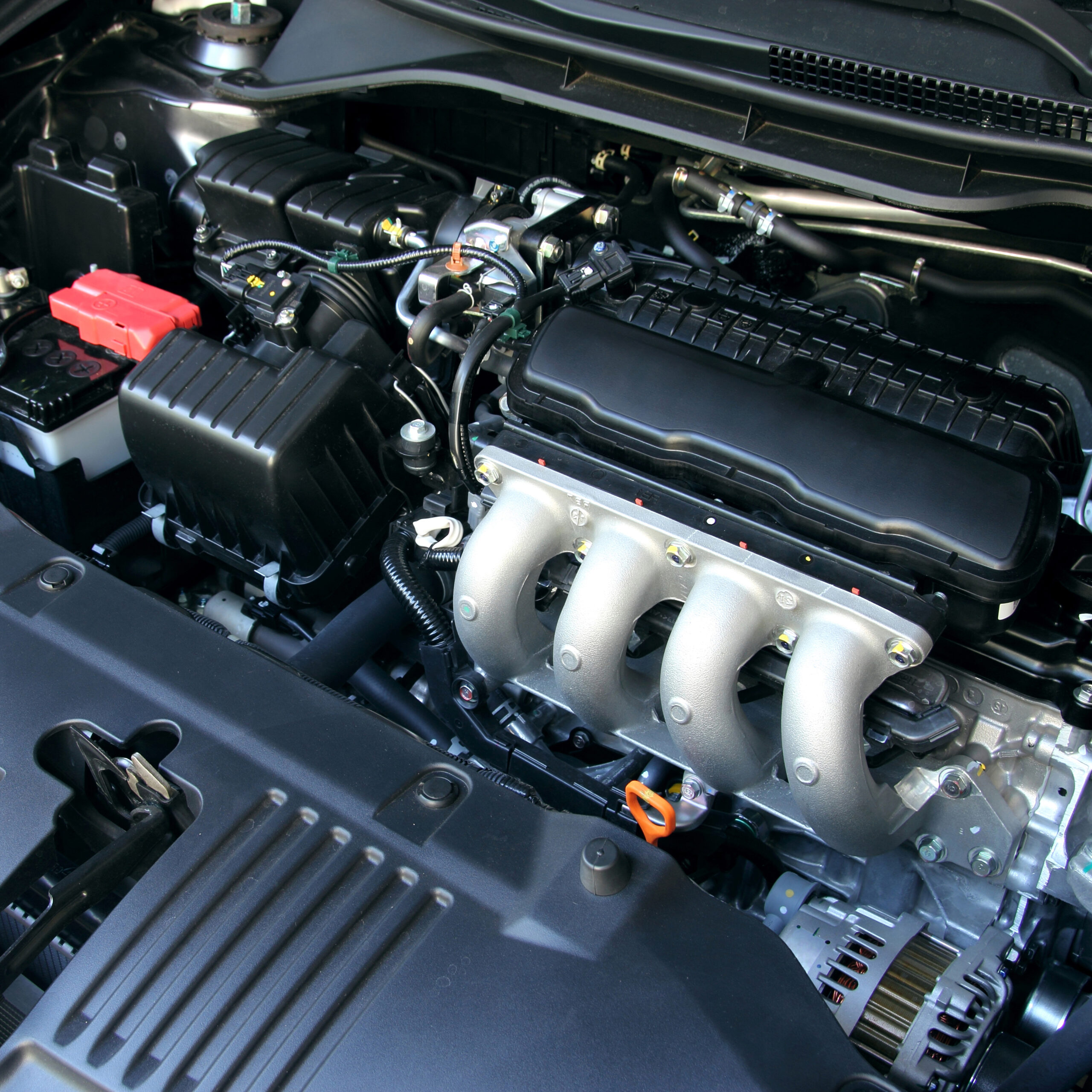 A close-up view of a clean car engine compartment, showing various engine components, including the intake manifold, air filter box, battery, wiring, and hoses.