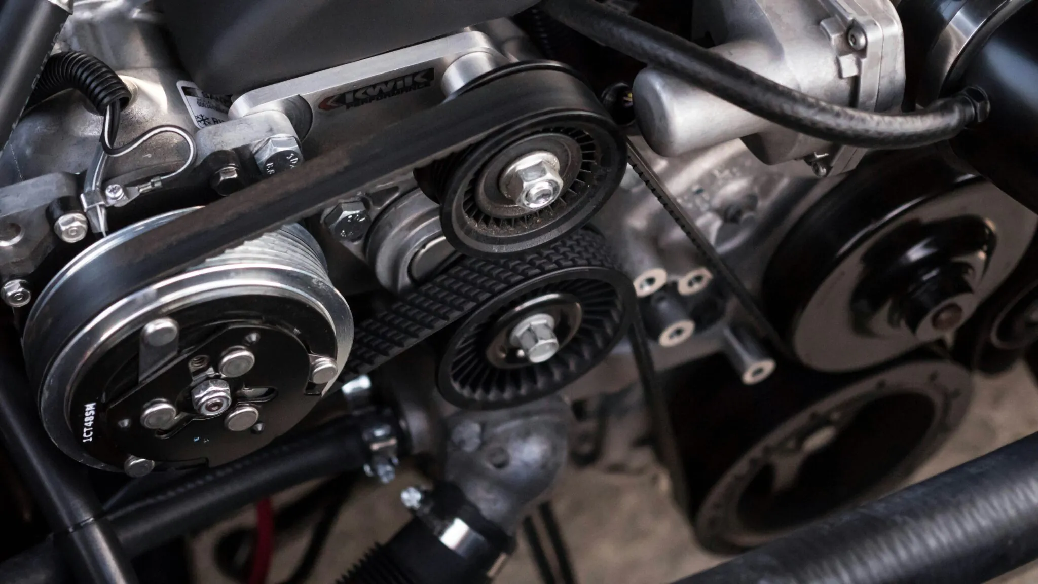 A close-up shot of a car engine, prominently featuring the drive belts, pulleys, and various engine components