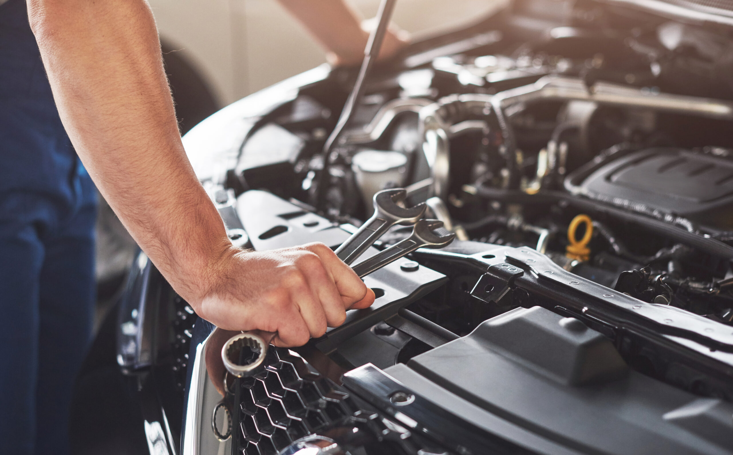 Mechanic inspecting car engine with a flashlight in garage